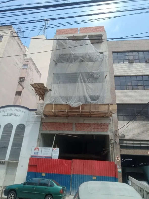 Fachada em execução com proteção de tela e fechamento provisório no térreo.