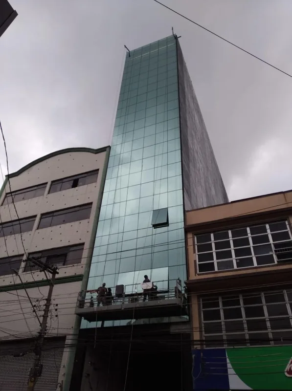 Edifício com volume vertical envidraçado, revestimentos e plataforma de trabalho.